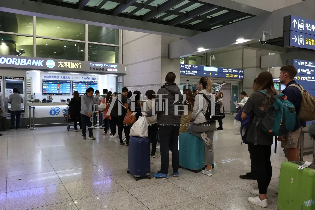 仁川空港のウリィ銀行両替カウンター前に並ぶスーツケースを引いた旅行者15名以上の長い行列