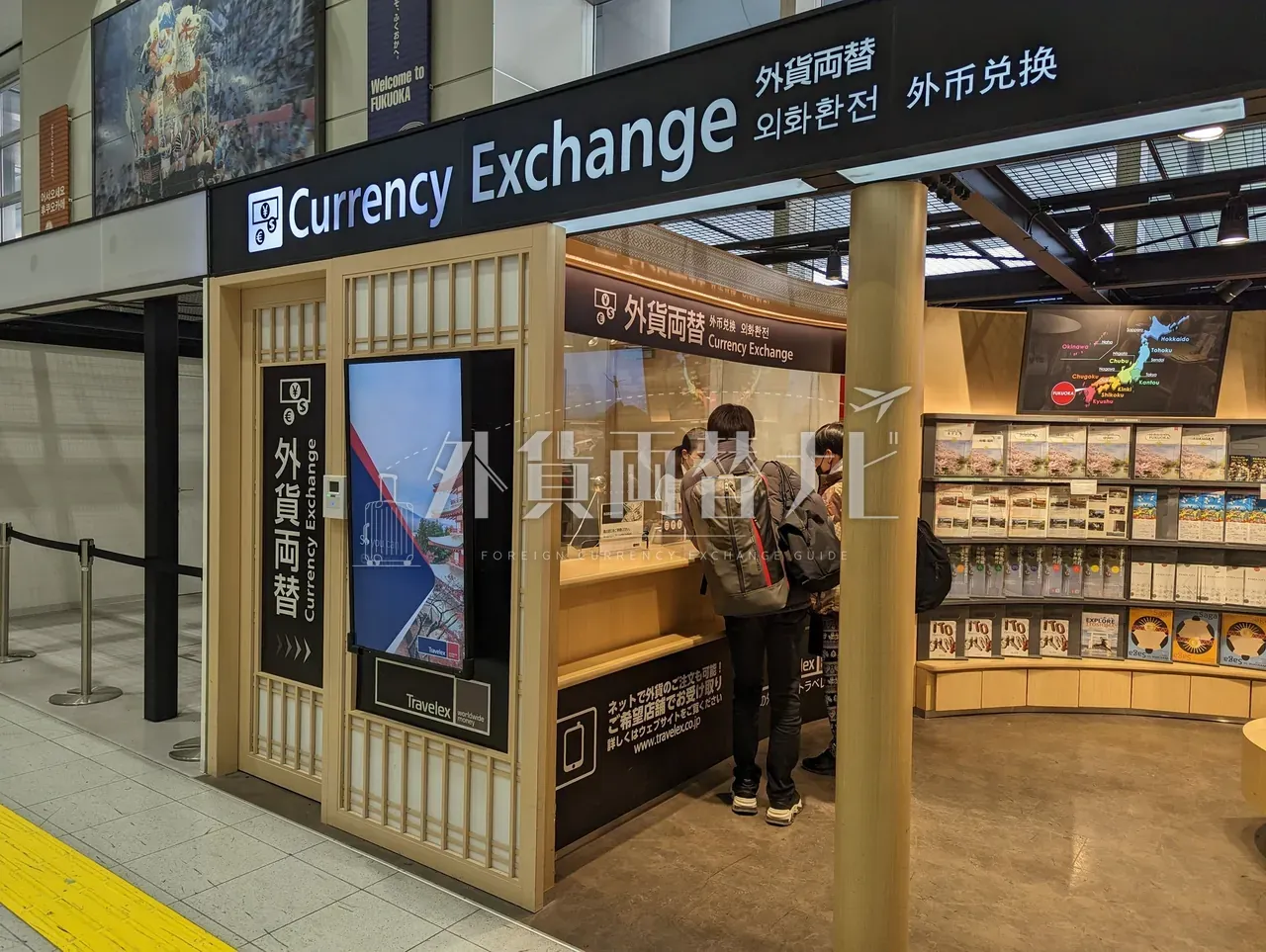 博多駅構内の和風木格子調 Currency Exchange カウンターで両替手続き中の観光客