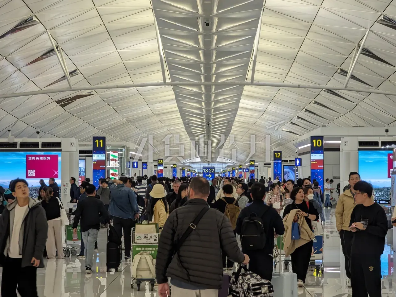 波形天井のアジアの空港出発ロビー、チェックインカウンターに大勢の旅客が並ぶ