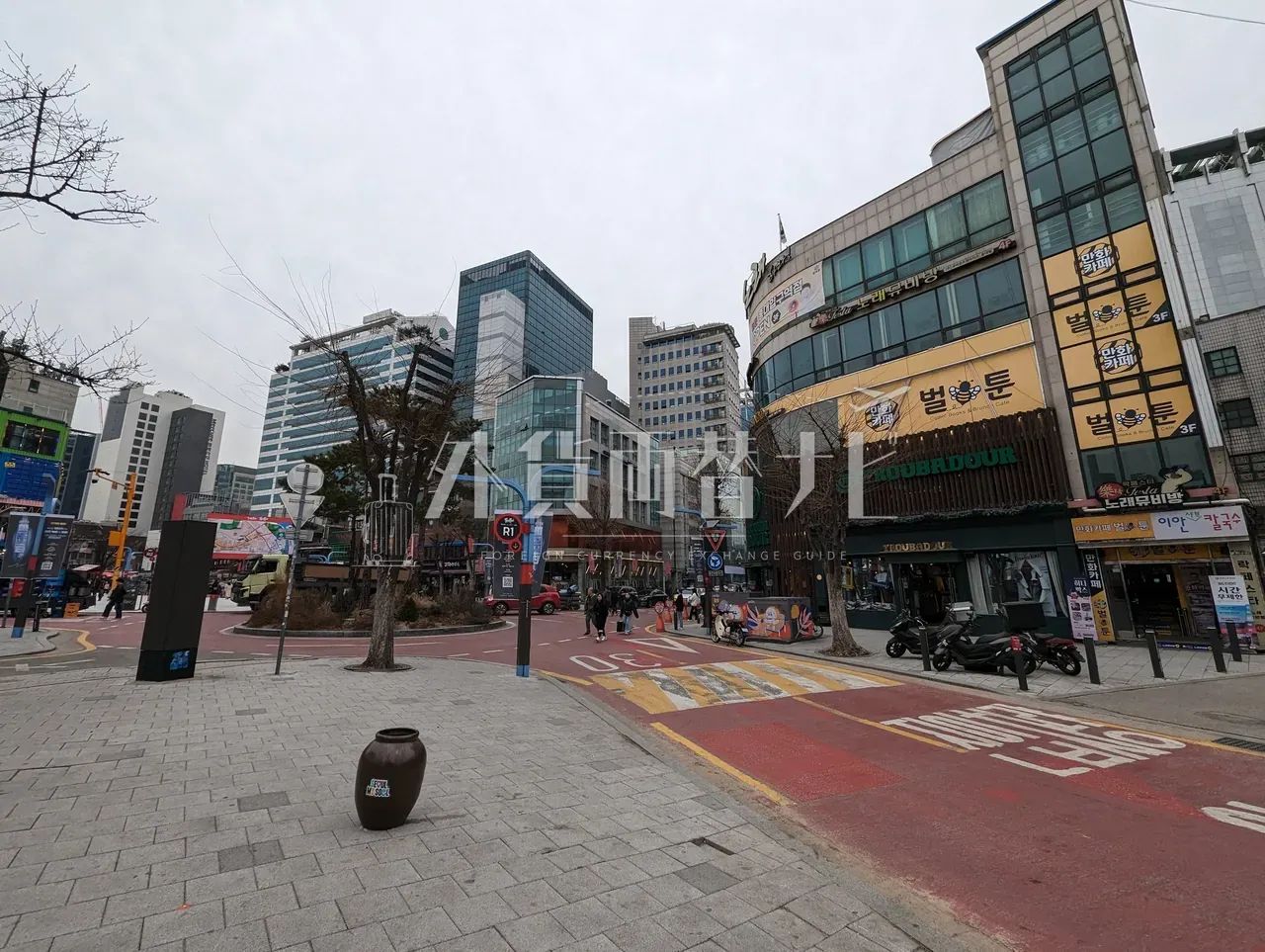 ソウル中心部の広場と歩道。曇天の中、観光客向け店舗が並ぶ通りの広角ショット
