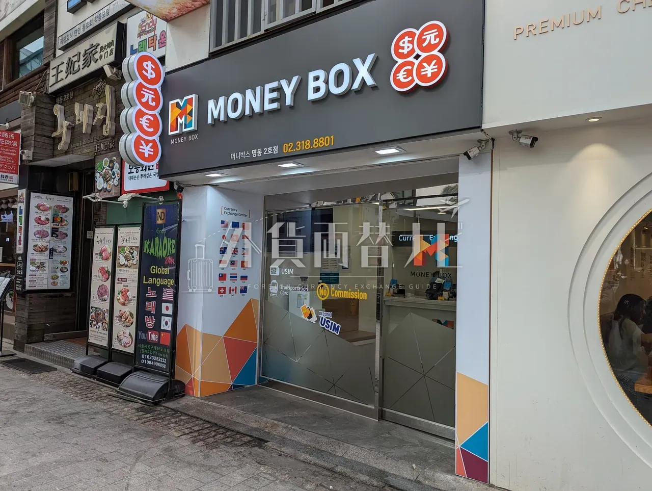 明洞のMoney Box店舗外観。黒地に白文字の看板と橙色のMロゴ、$元€¥通貨記号ラベル
